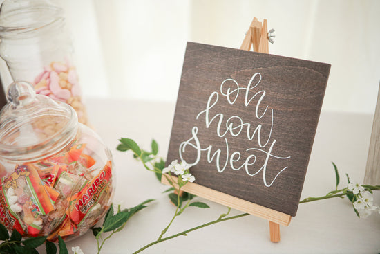 Wedding sweet table decoration saying ‘oh so sweet’, painted with calligraphy onto grey wood