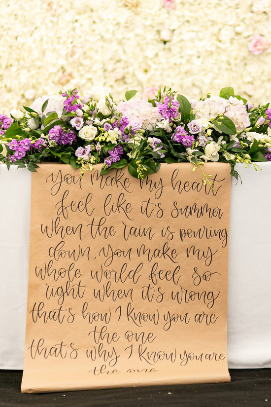 Kraft paper scroll hanging from top table at Essex wedding. Hand Lettered in brush calligraphy with first dance song lyrics