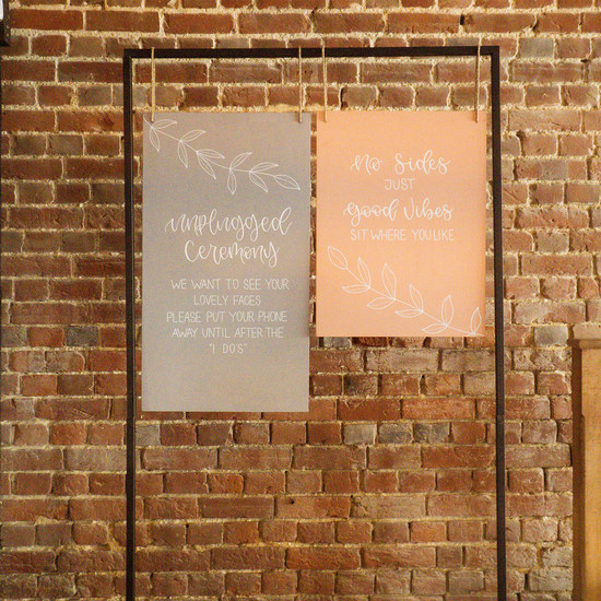 Hanging wooden wedding sign with unplugged ceremony hand lettered. Next to pink hanging sign with no sides ceremony detail