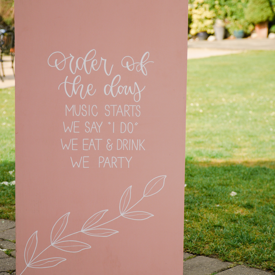 Order of the day wedding sign painted in pink tones for spring wedding at a Kent wedding venue